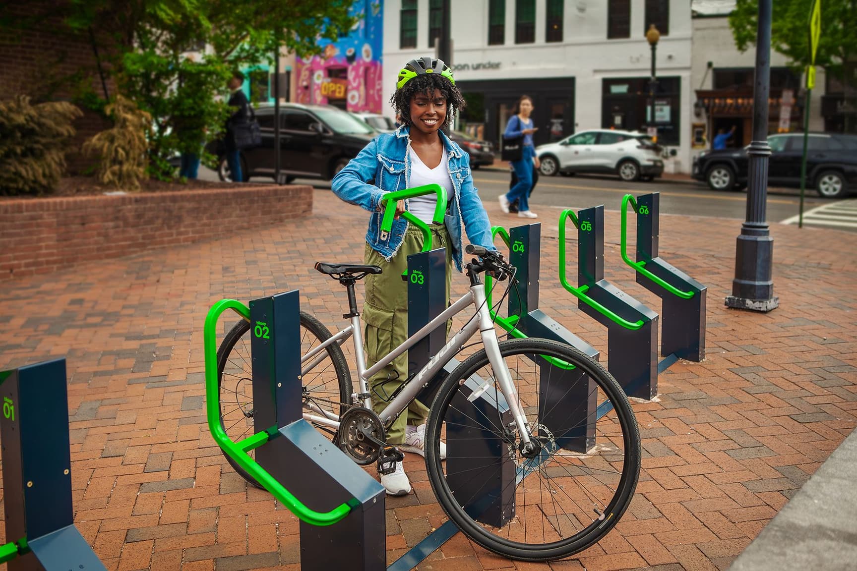 Smiling cyclist at Bikeep smart parking station on a tree-lined downtown street, USA